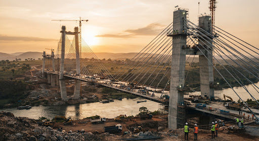 Cable-stayed bridge under construction at sunset with crews on site