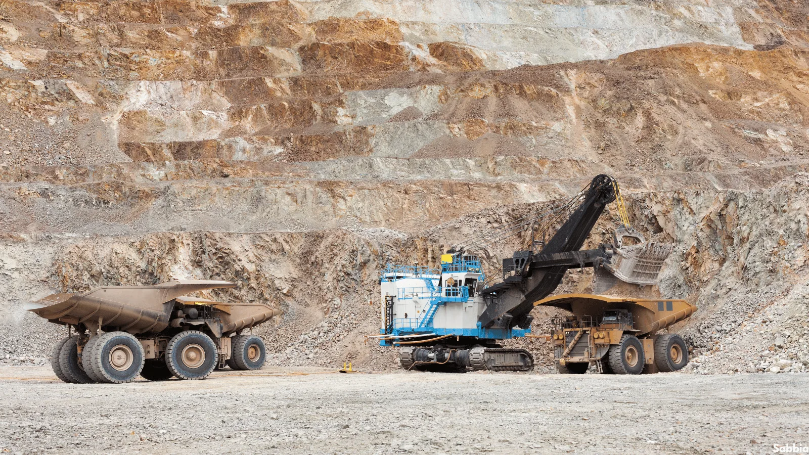 Excavator loading haul trucks at an open pit mine, representing the mining and logistics division of Sabbia International